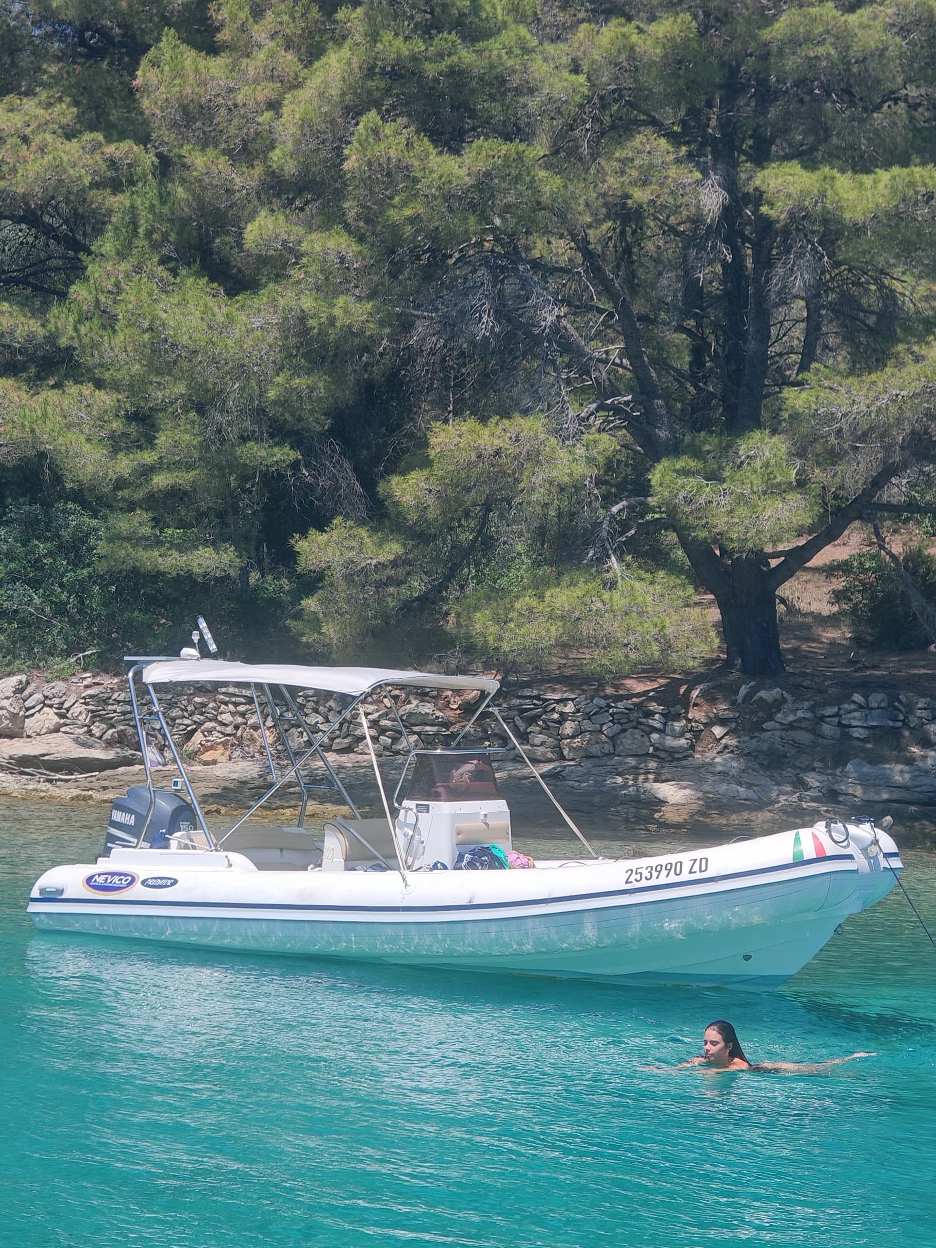 Motorboat anchored off Adriatic pine coast with swimmer nearby