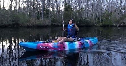 Solo kayaker gliding at dusk on reflective backwater river