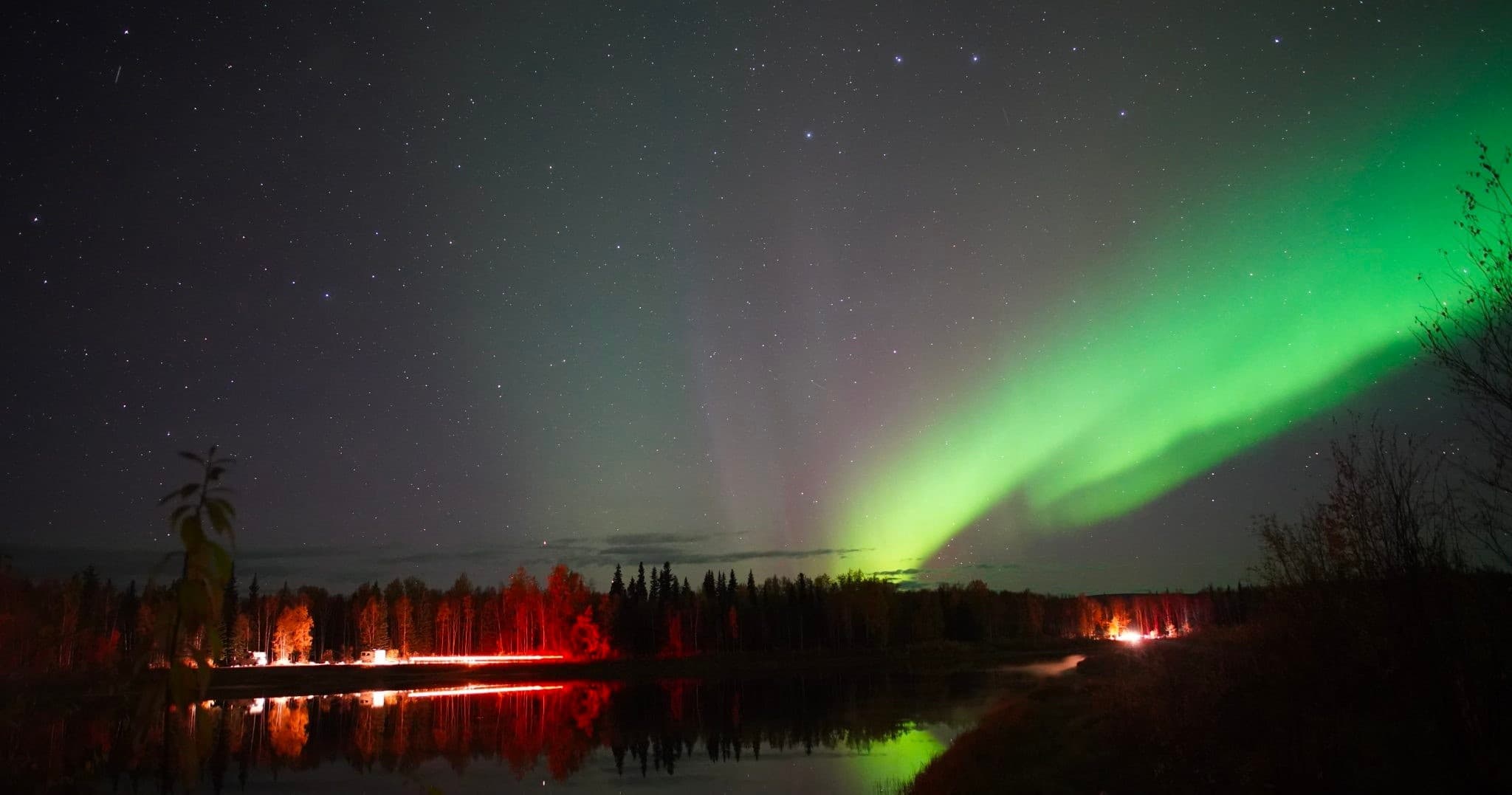 Northern lights over reflective lake and forest at night