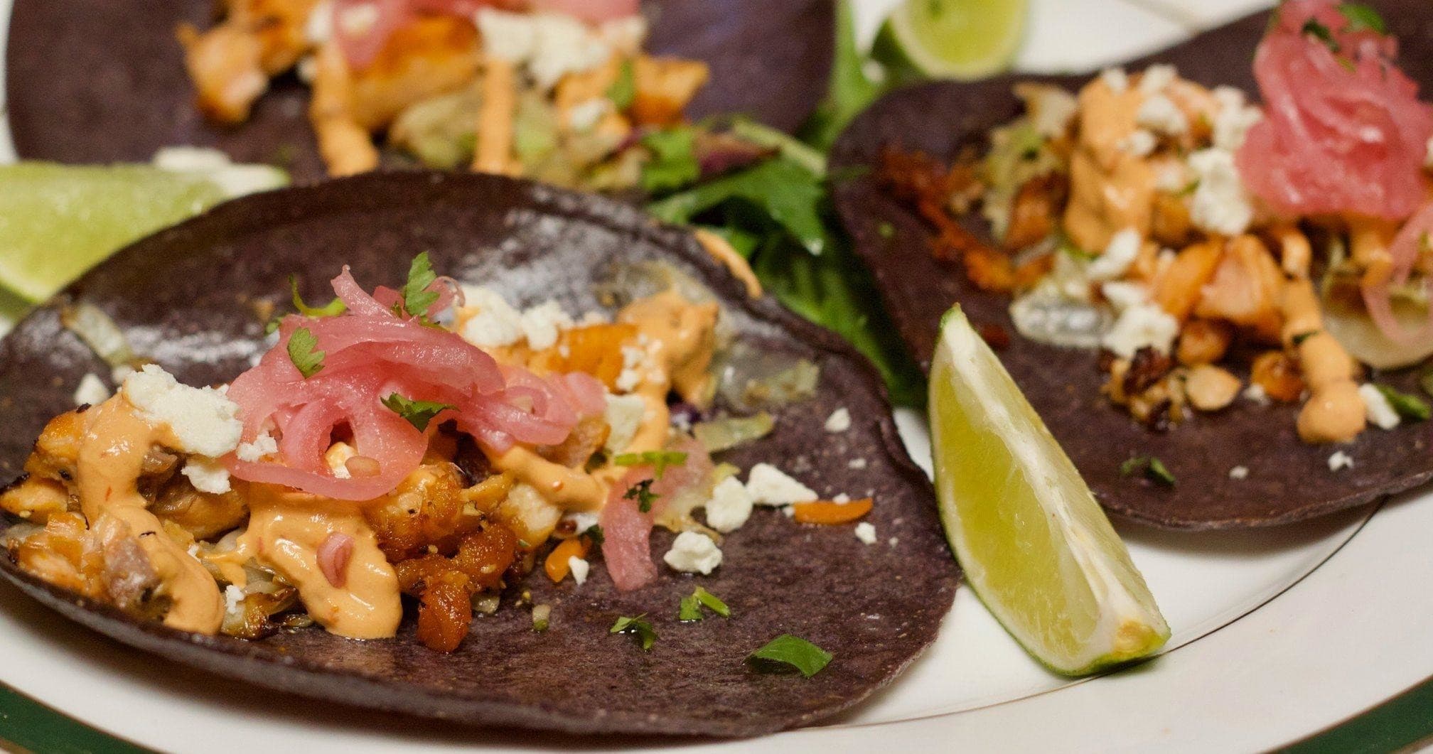 Black-tortilla seafood tacos plated with lime, close-up dining