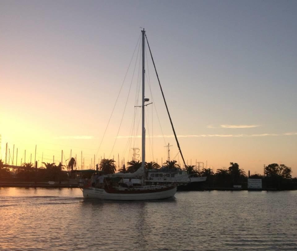 Sailboat silhouetted at sunset on calm coastal harbor