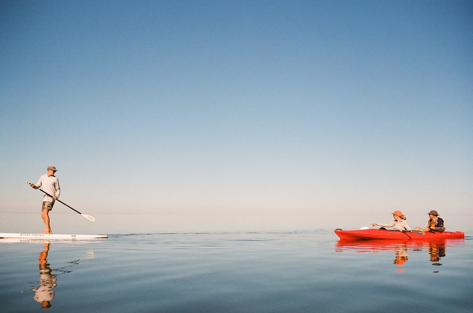 Paddleboarder and kayakers on calm ocean with wide horizon
