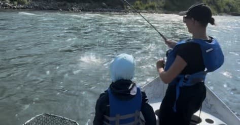 Guide and angler battling trout on fast-moving river from drift boat
