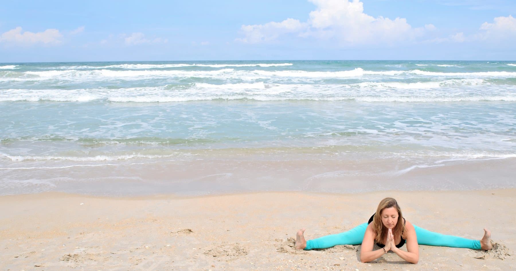 Seaside yoga split on sandy beach with ocean waves