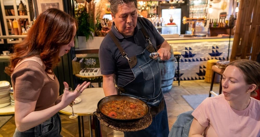 Server presenting paella to diners inside Barcelona tapas restaurant