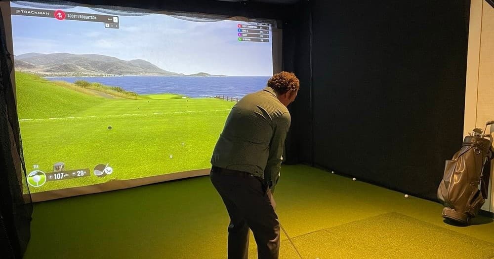 Golfer practicing swing in indoor simulator on coastal course