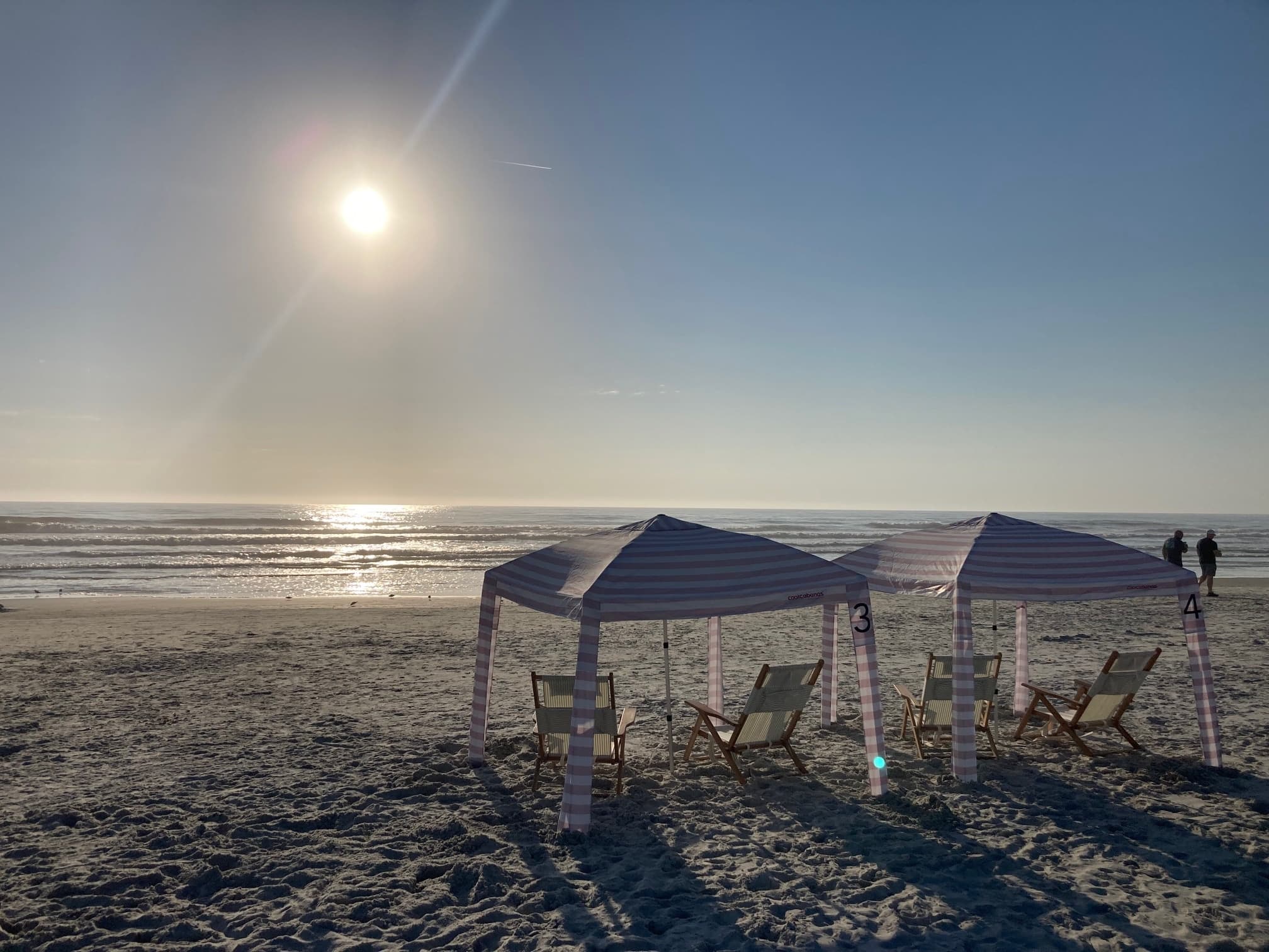 Sunset over beach with shaded cabanas and tranquil surf