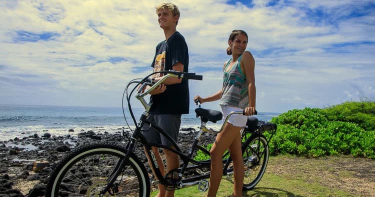Couple riding electric cruiser bikes along coastal shore in Hawaii