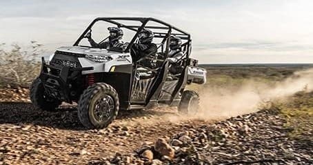Four-seat UTV racing across open desert plain, dust trail