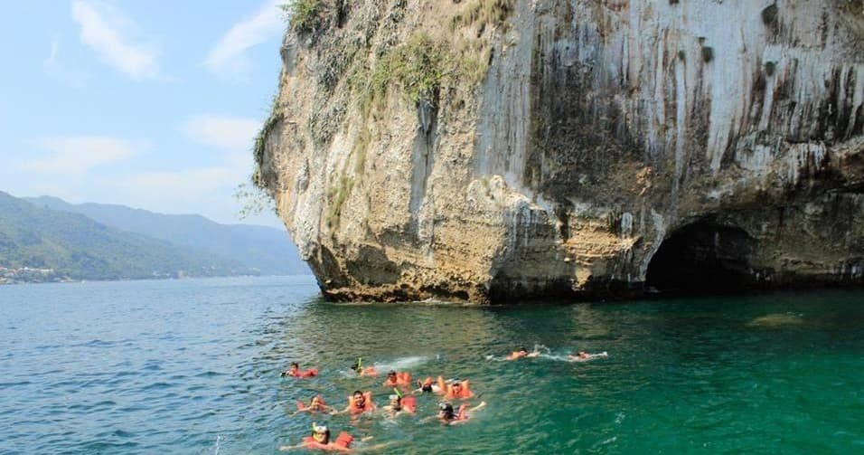 Snorkelers swimming near dramatic coastal cliff and sea cave