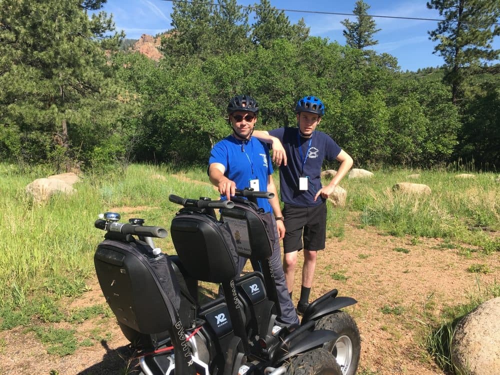 Two participants with Segways on grassy canyon trail, smiling