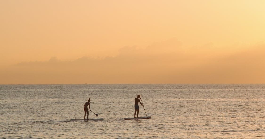 Two paddleboarders gliding at golden sunset across calm sea