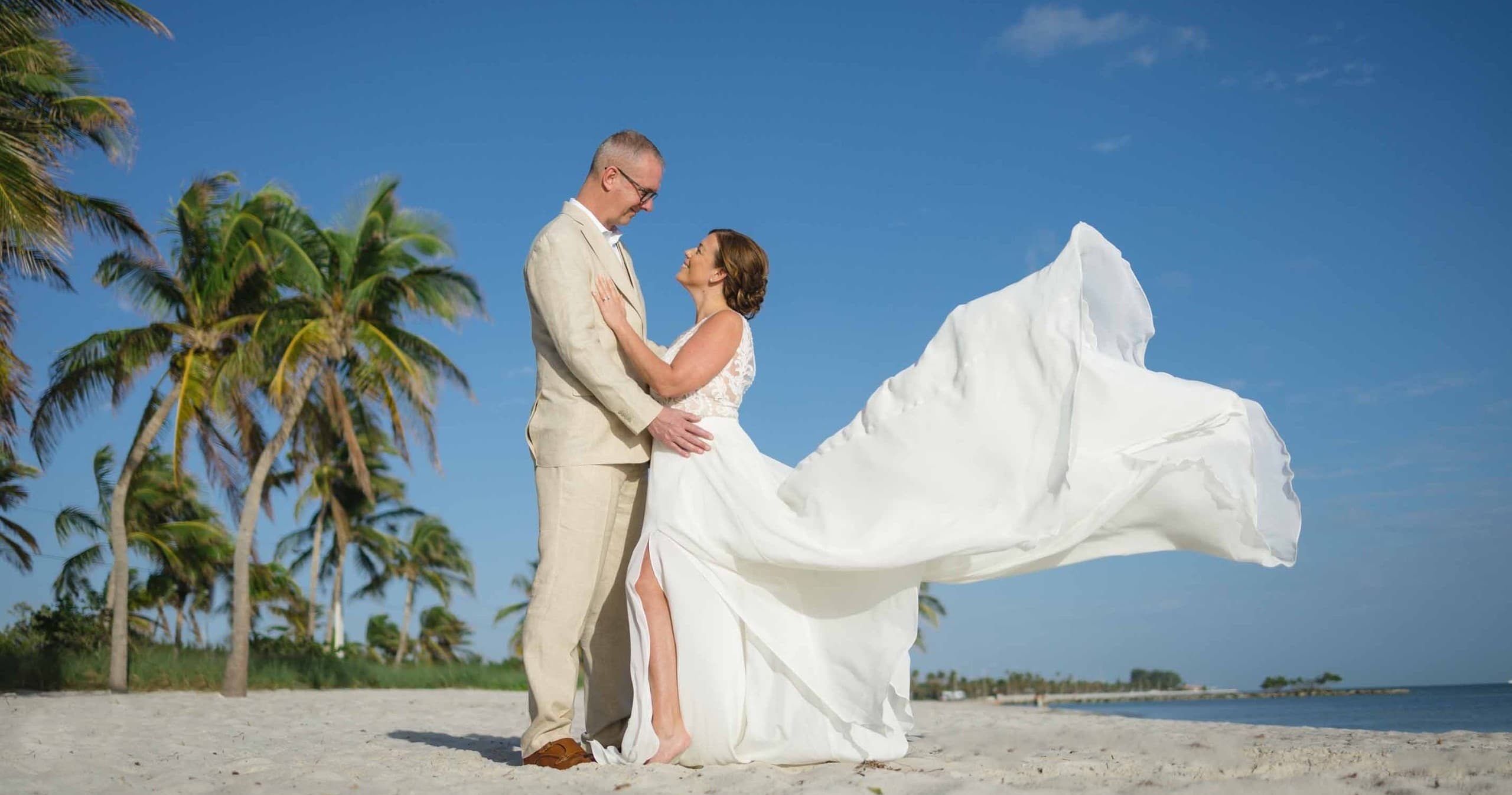 Bride and groom on beach with flowing gown and palm backdrop