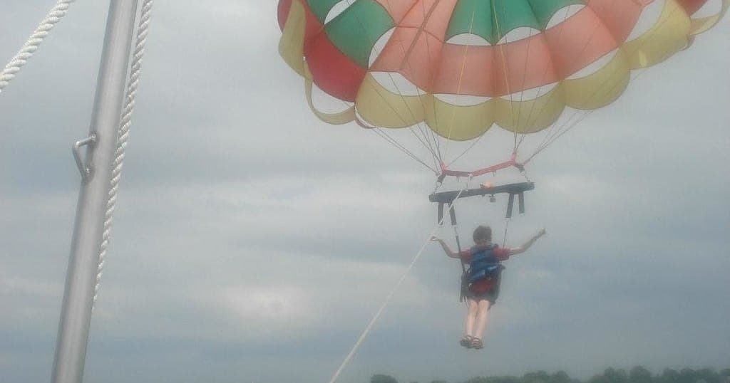 Parasailer suspended from boat under cloudy sky over lake