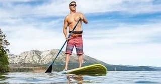 Stand-up paddleboarding near mountain lake with clear skies