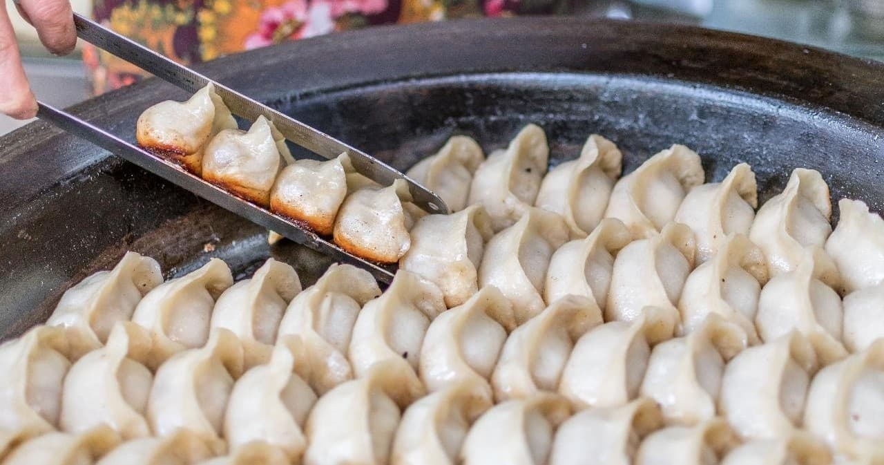 Chef frying dumplings on large pan at busy street food stall