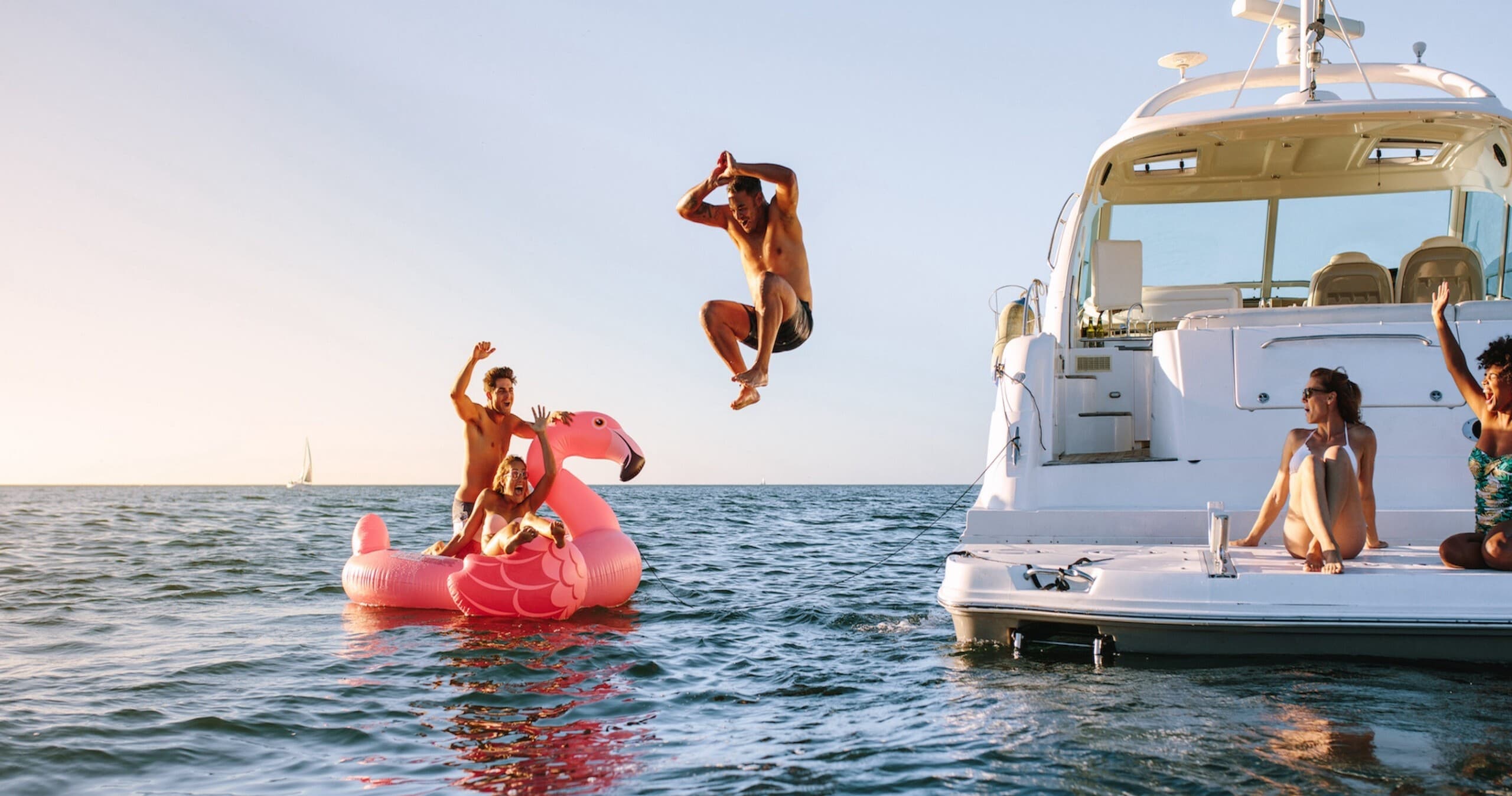 Group jumping from yacht into open ocean near sunset on summer charter