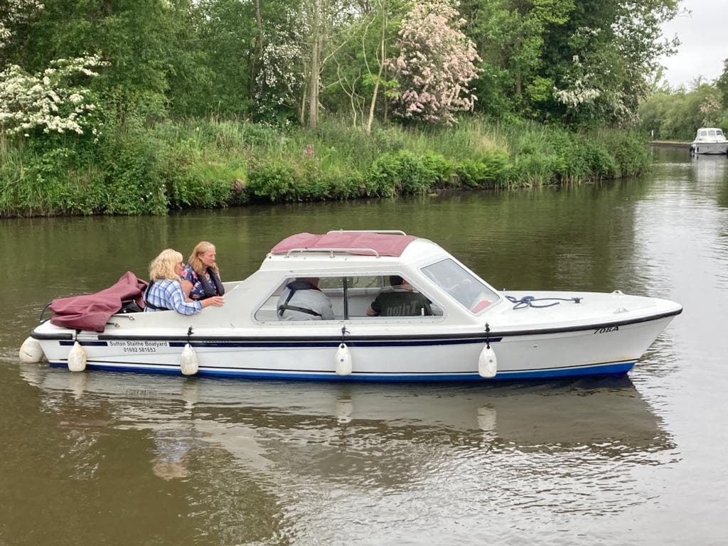 Small motorboat cruising a calm river with passengers and woodland