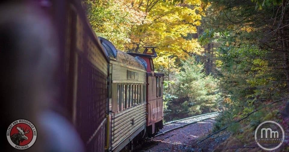 Vintage train winding through colorful fall forest near Maine lake