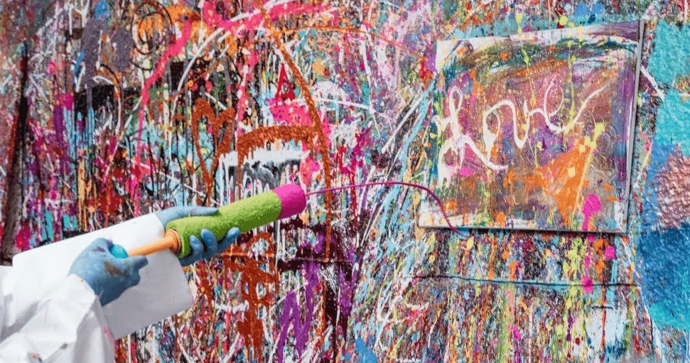 Participant spraying colorful paint on studio wall during paint party