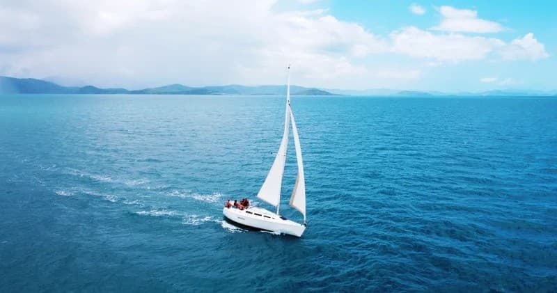 White sailboat sailing on deep blue ocean under clear sky