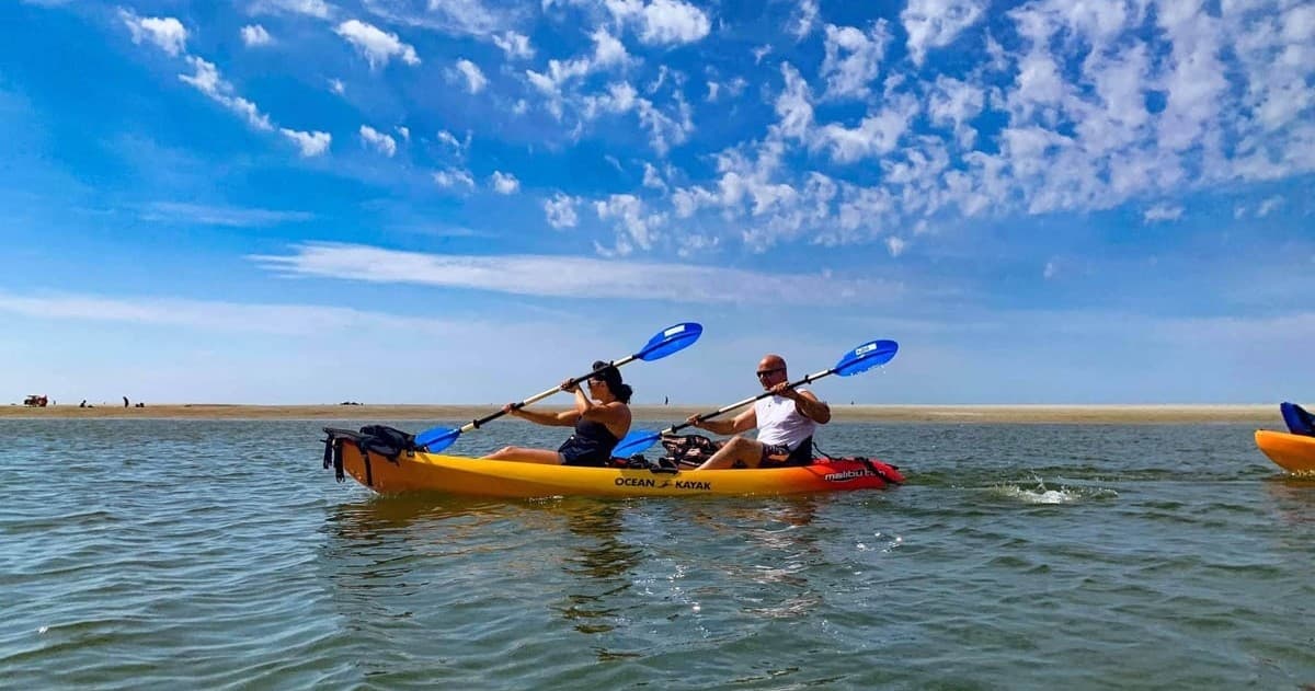 Two kayakers paddling across open coastal water under sky