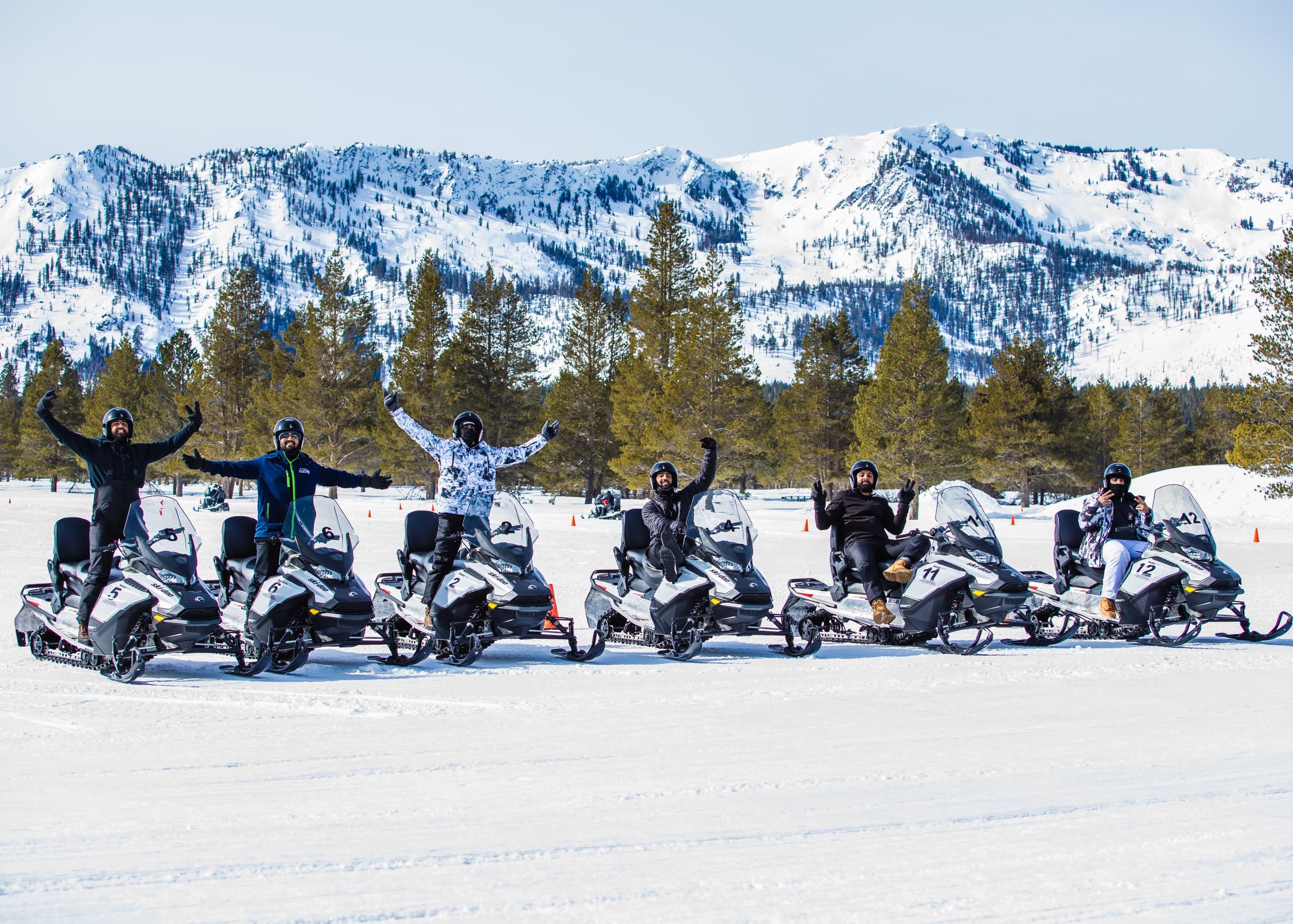 Snowmobile tour group lined up on snowy lake with mountain vista