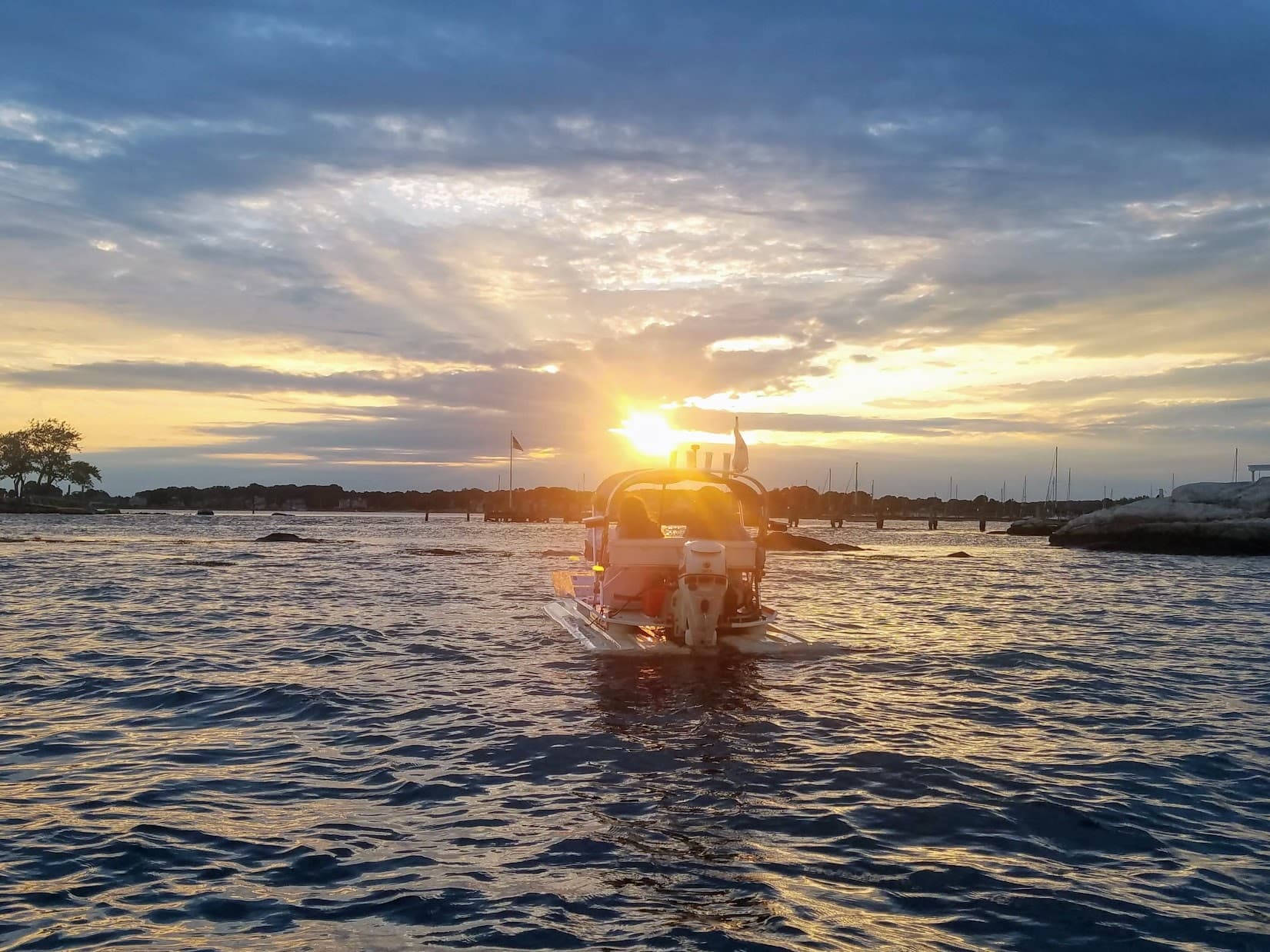 Powerboat cruising toward marina at sunset on calm coastal waters