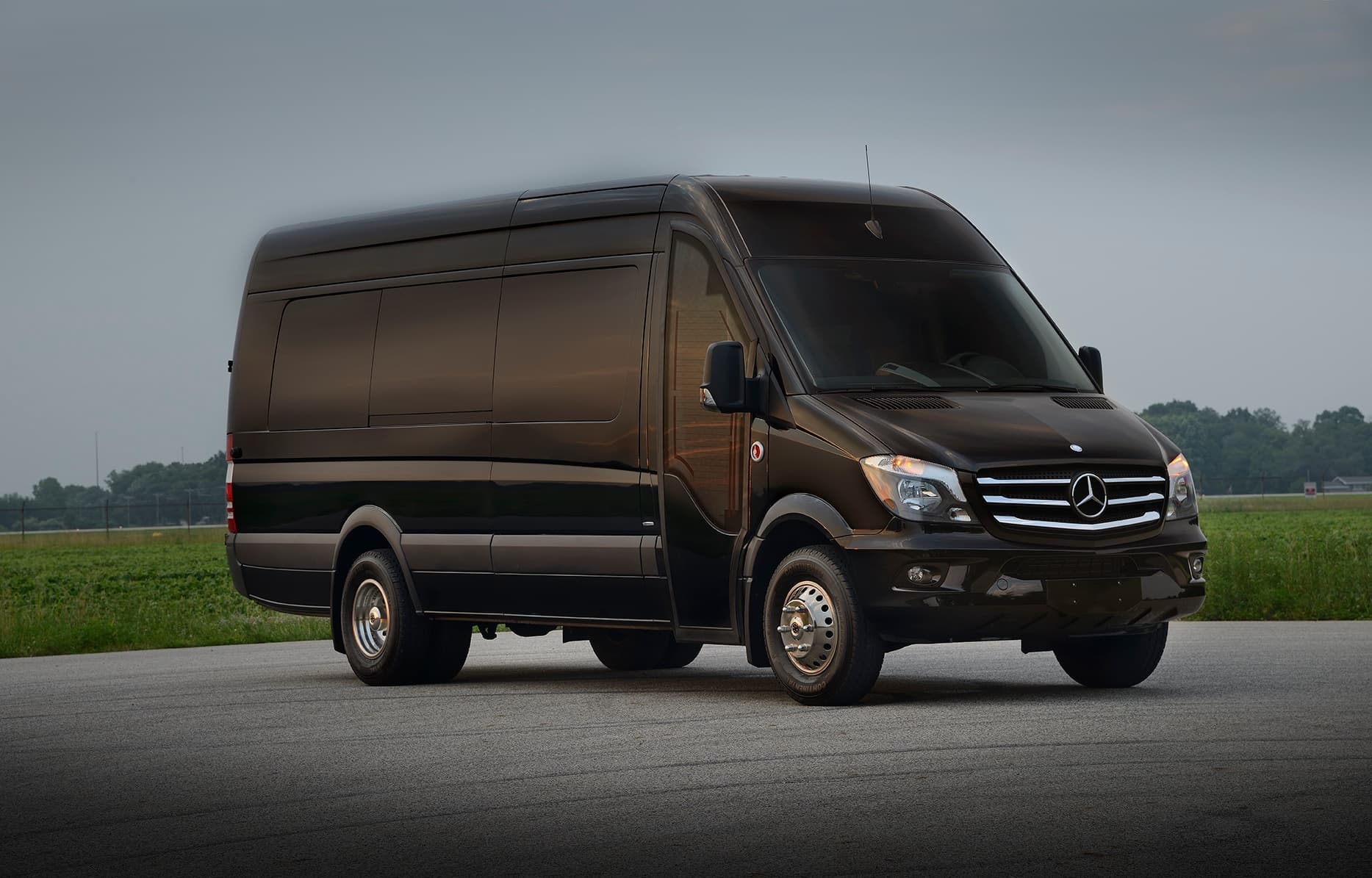 Black luxury shuttle van parked on open road with fields
