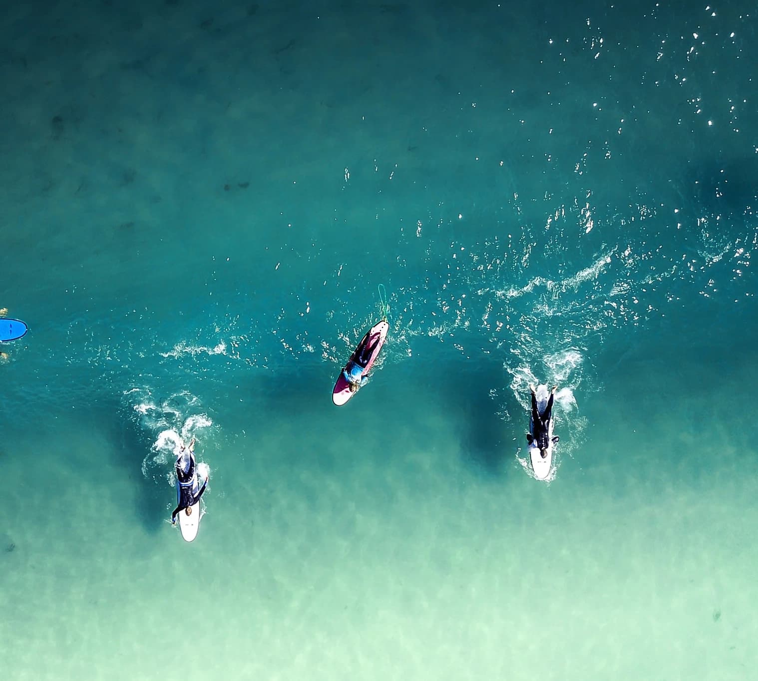 Aerial shot of three surfers riding small waves in coastal water