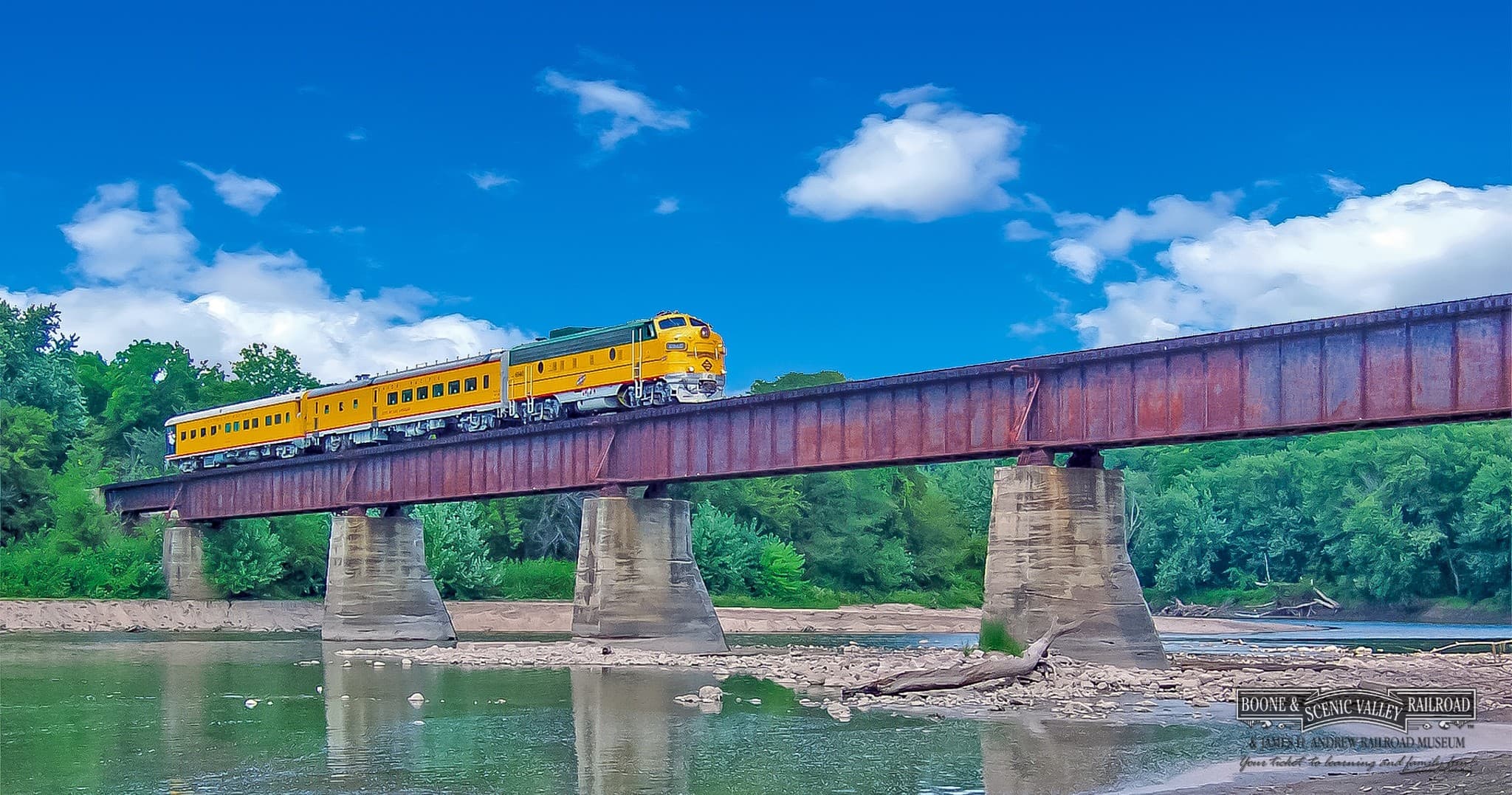 Vintage train crossing river bridge beneath blue summer sky