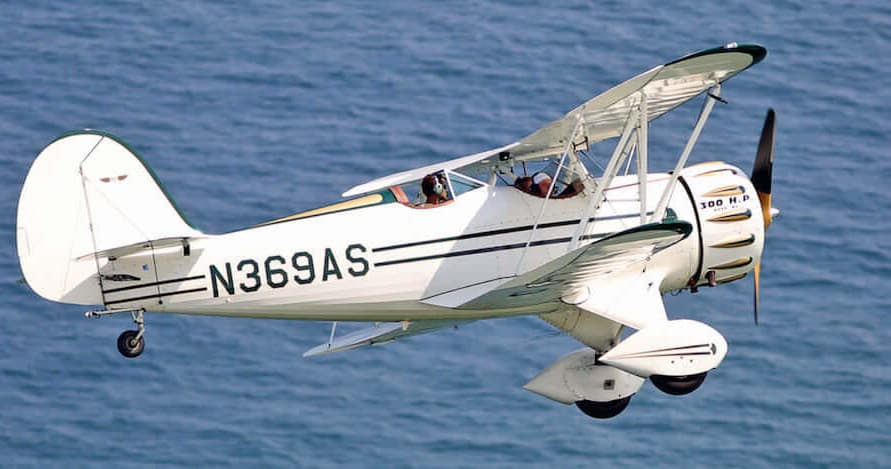 Vintage biplane flying low over open ocean near coastline