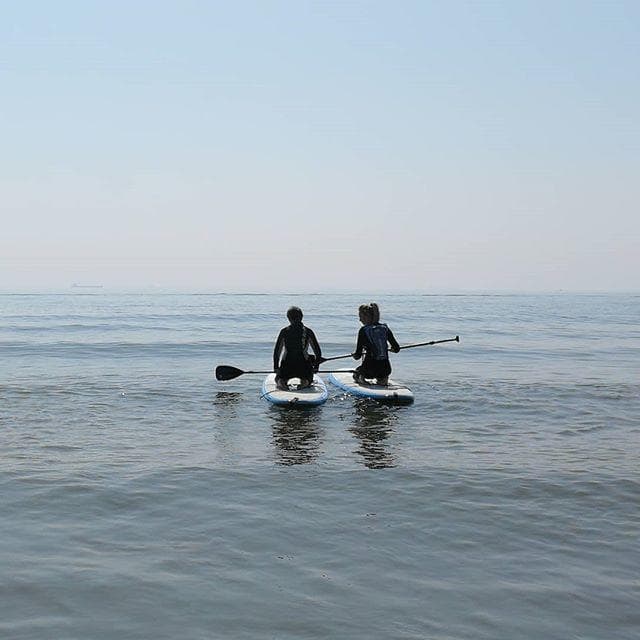 Two paddleboarders sitting on calm sea at coastal horizon