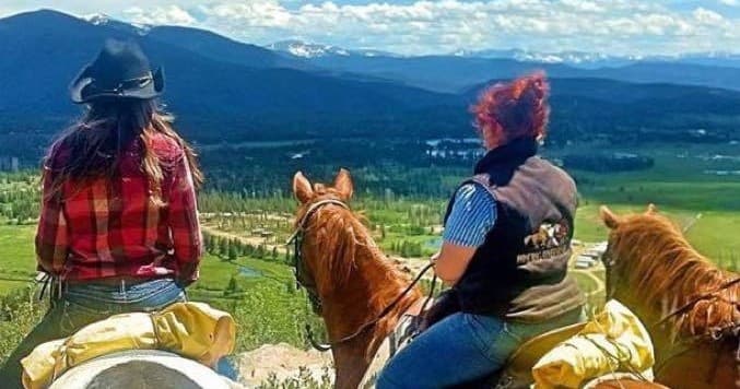 Two horseback riders overlooking mountain valley on scenic trail