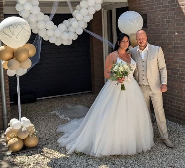 Outdoor wedding couple posing by balloon arch at venue entrance