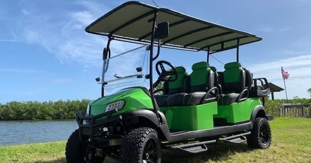 Green rental golf cart parked on coastal grassland near water