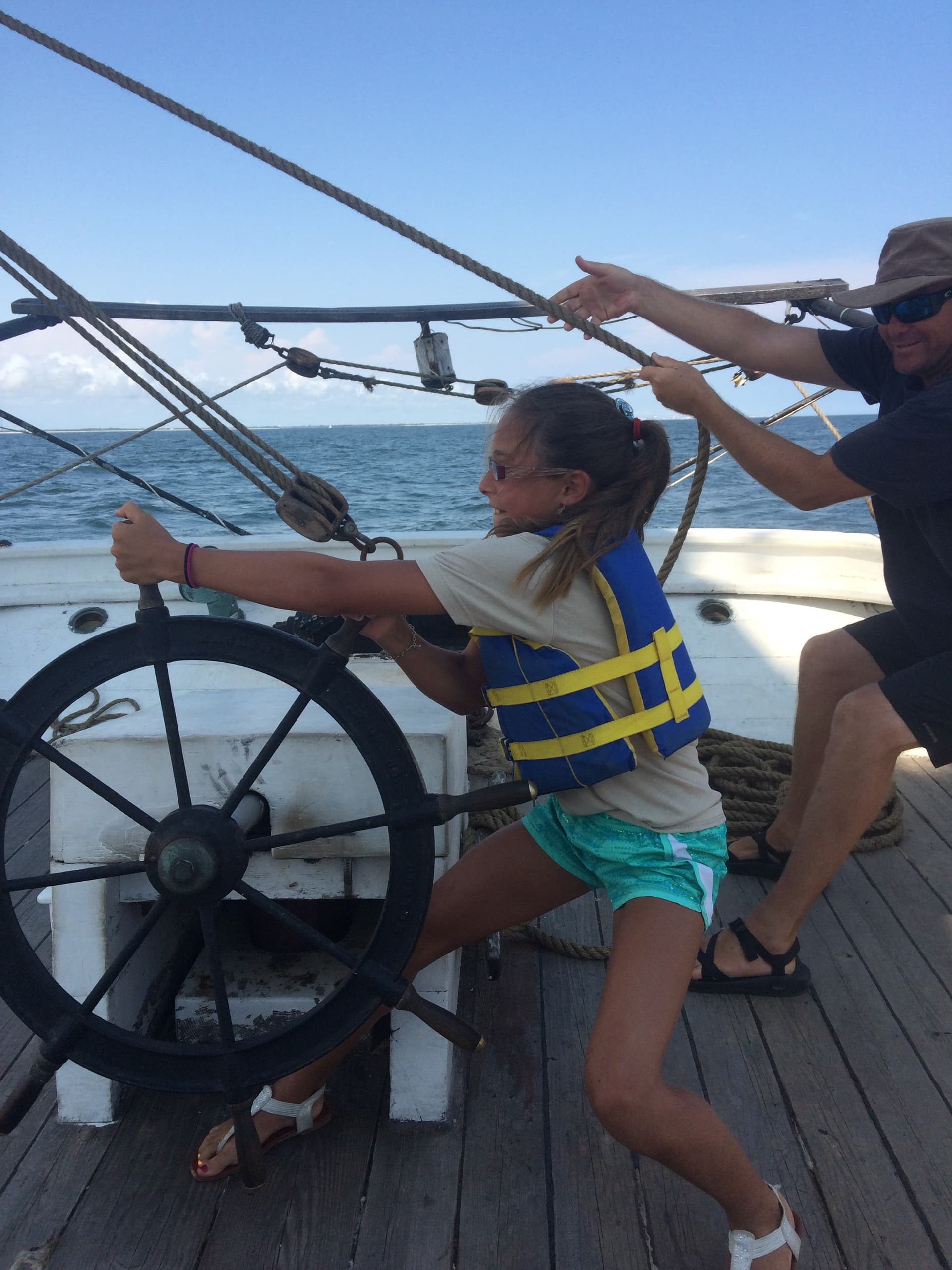 Child steering ship wheel on deck during family sail adventure