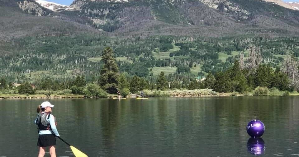 Paddler standing by buoy on calm mountain lake with forest