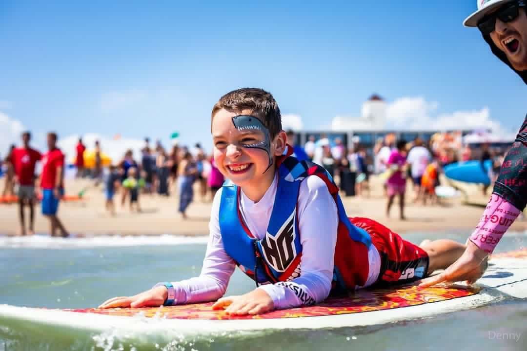 Smiling child on surfboard at crowded beach surf festival