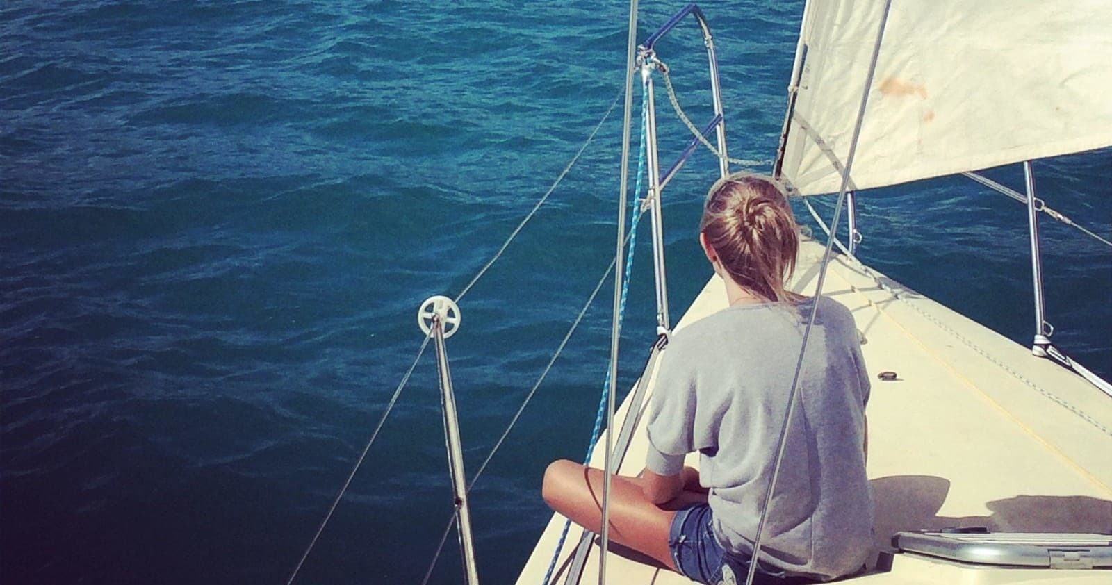 Skipper seated on bow of sailboat enjoying calm ocean vista