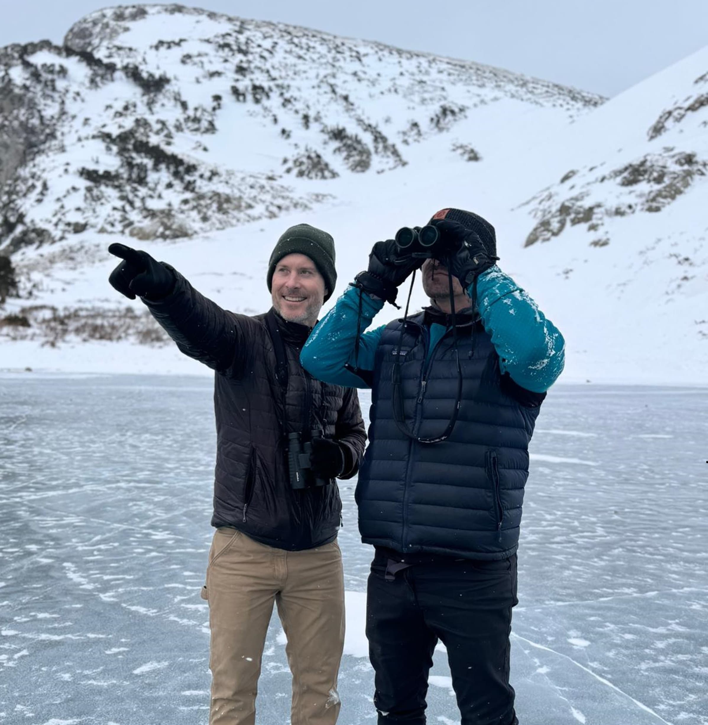 Two men pointing and birding on frozen alpine lake in winter
