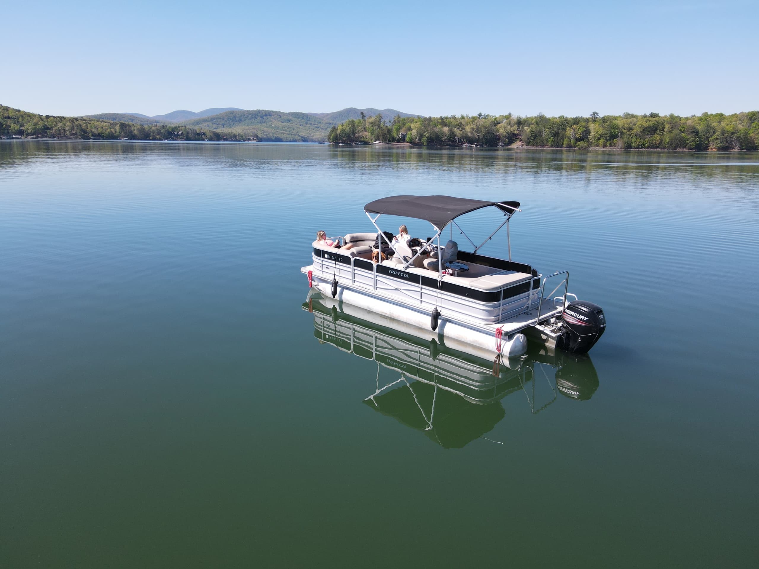 Aerial pontoon boat on glassy lake with distant forested shore