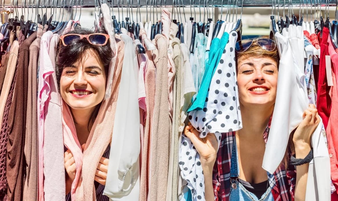 Two women browsing clothing racks in bright indoor market