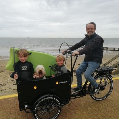 Parent and children on cargo bike riding along sandy beach