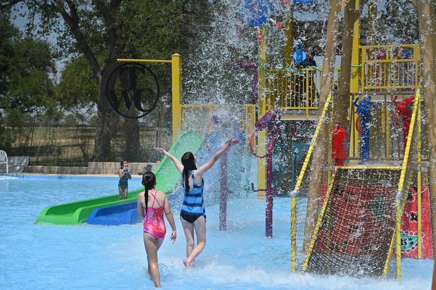 Children playing under splash pad buckets at outdoor waterpark
