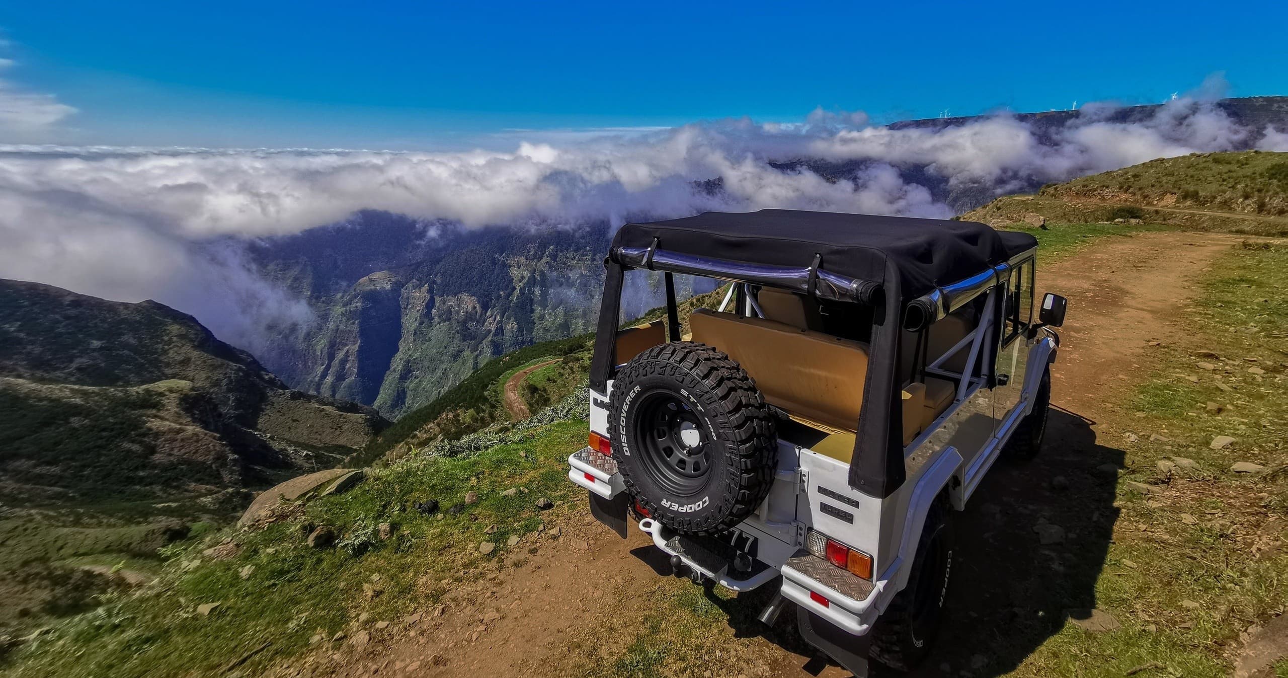 Open-top 4x4 on coastal cliff edge with cloud inversion