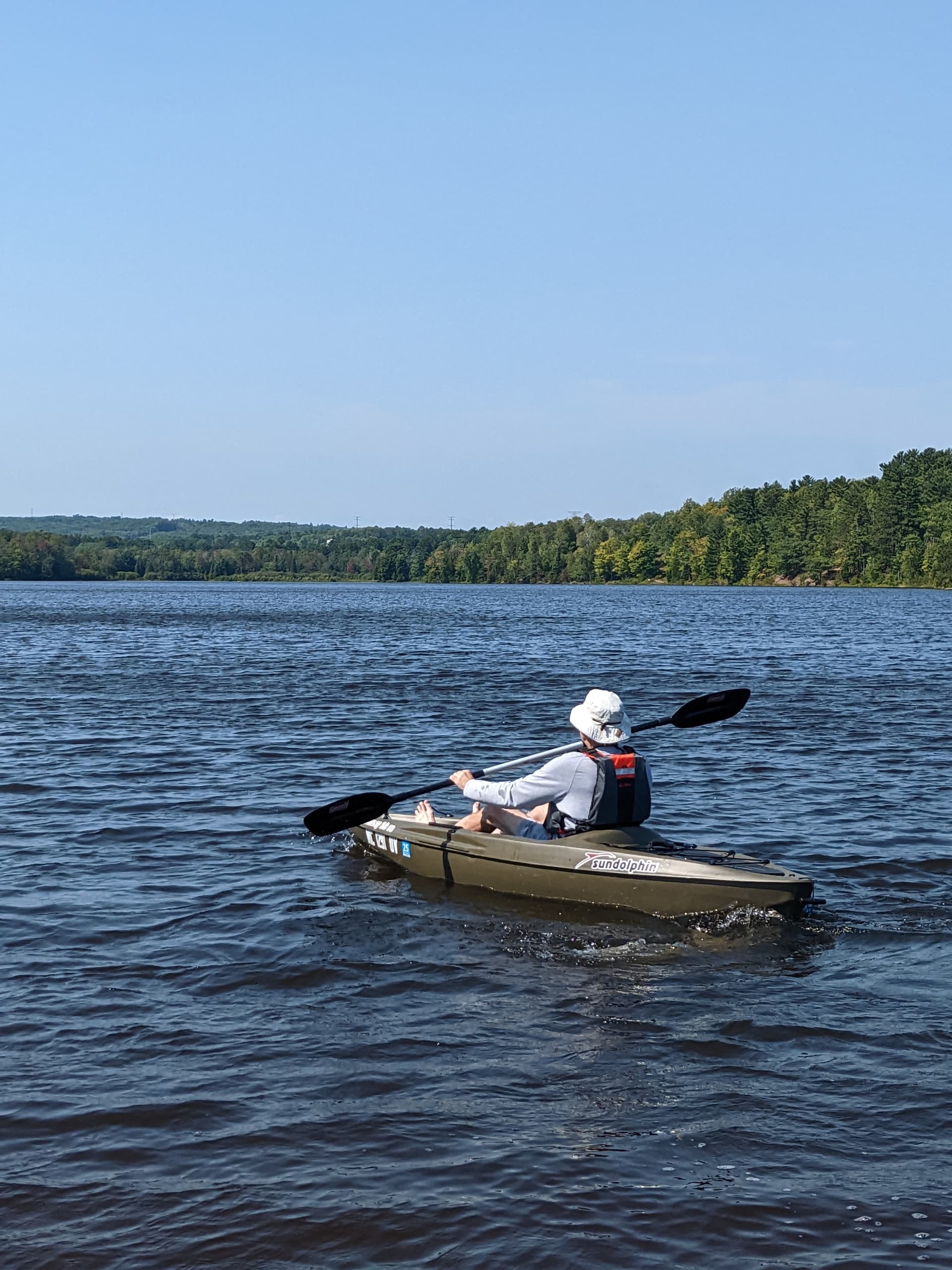 Solo kayaker paddling on wide inland lake under clear sky
