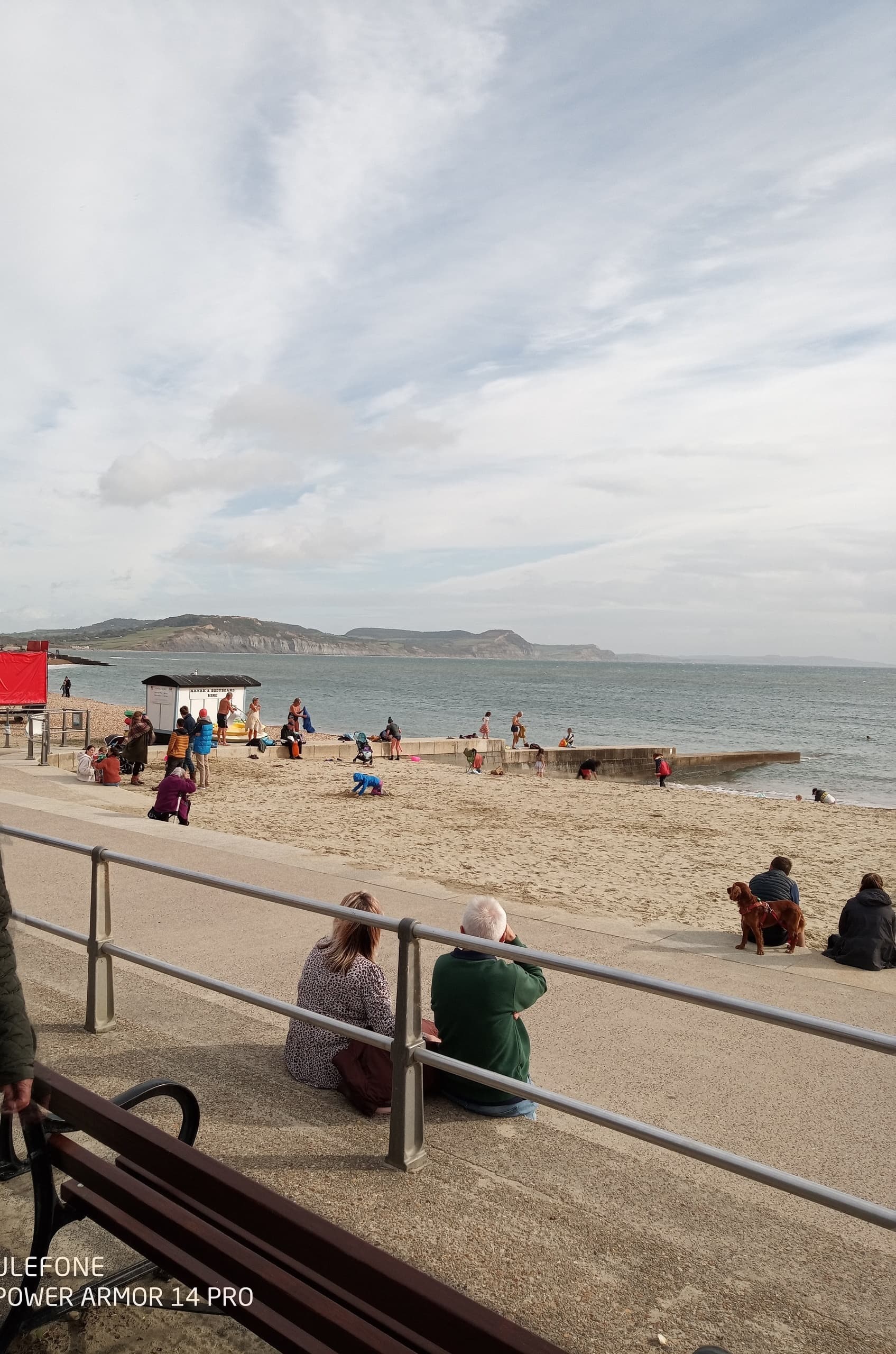 Visitors sitting on seaside promenade overlooking sandy beach