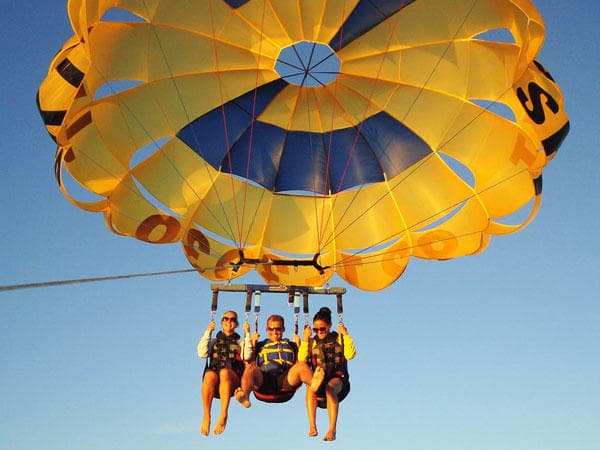 Three people parasailing under yellow canopy over open ocean sky