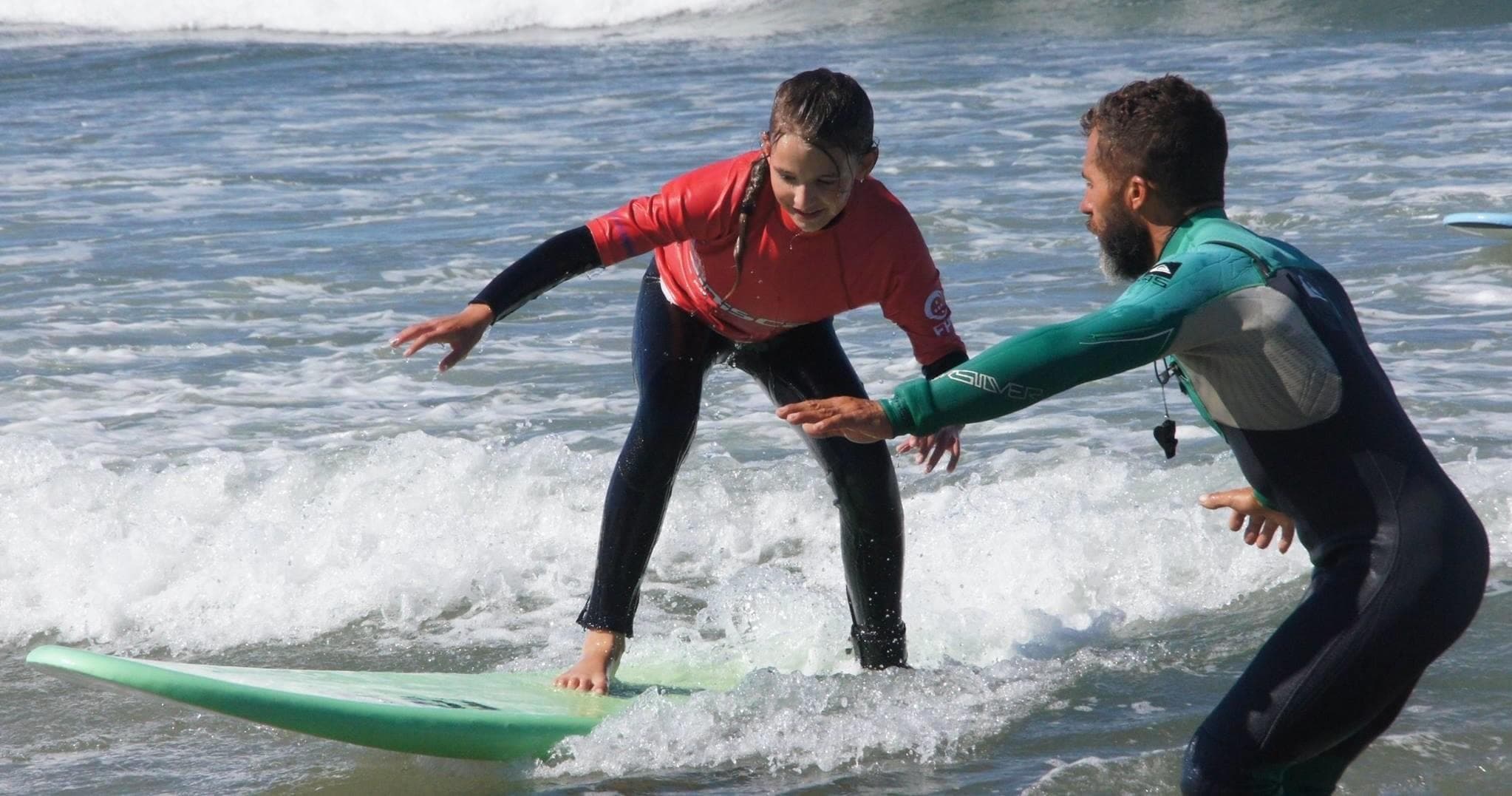 Surf instructor coaching student riding small wave on beach